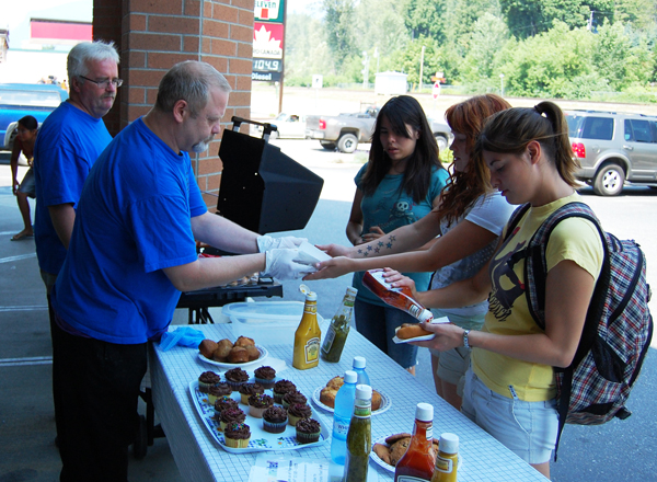 Volunteers Tim Butcher (left) and Terry Aarnoudse served up some pretty tasty dogs to Breanna Howe, Rochelle Morgan and Megan Howe at Pharmasave's fund-raising barbecue to benefit the Community Connections Food Bank on Friday. Community Connections' Patti Larson said the fund raiser was very successful. David F. Rooney photo