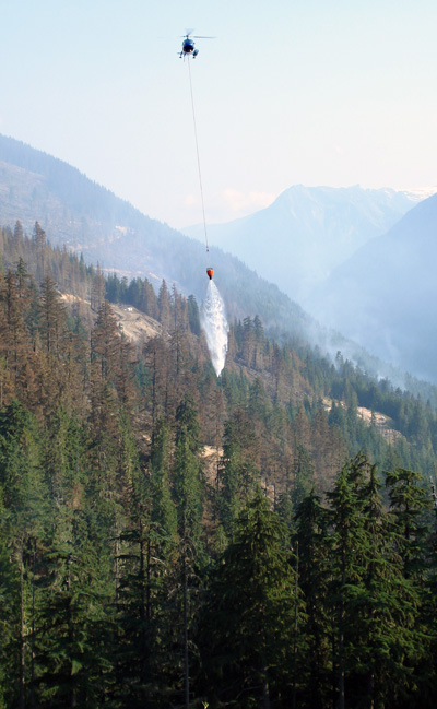 A helicopter buckets a a burning stand of trees at the Perry River Fire. Photo courtesy of Ben Parsons