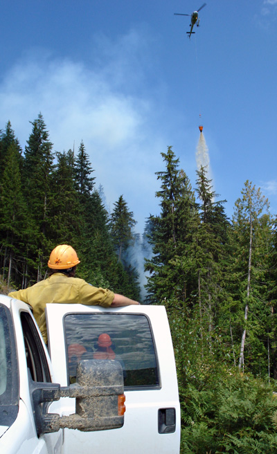 An unidentified Nakimu firefighter watches from a truck as a chopper buckets part of the Perry River Fire. Photo courtesy of Ben Parsons