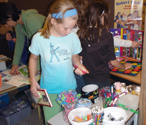 Erin Behncke looks at the pens, pencils, erasers and other neat things for sale after picking her book during the annual Arrow Heights Elementary School Book Fair. Photo by AHE student photographer Jacqueline Cottingham 