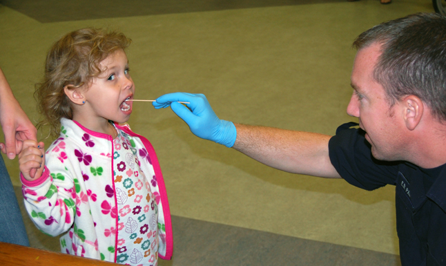 Open wide! Ava Lund peers sideways at a photographer as RCMP Const. Eric Page take her DNA sample with a swab. All of the data gathered at the event was entered into booklets that were given to parents for safekeeping. The Mounties kept nothing for themselves. David F. Rooney photo