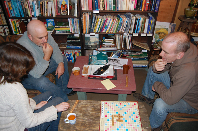 Gwen Lips (left) waits as her opponent Chris Johnston (right) as he, mimicked by onlooker Andrew Stacey (upper left), ponders his next word during an evening of Scrabble at Castle Joe Books on Thursday evening. Lips, who owns the small book store on Second Street West, plans more evening events, including more Scrabble, this winter. David F. Rooney photo