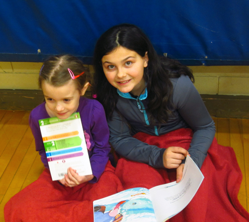 AHE students Haley Speidel and Cassidy Legebokow are sharing their books for the buddy read in the Arrow Heights Elementary gym. Photo by AHE Student Reporter-Photographer Alice Dunkerson