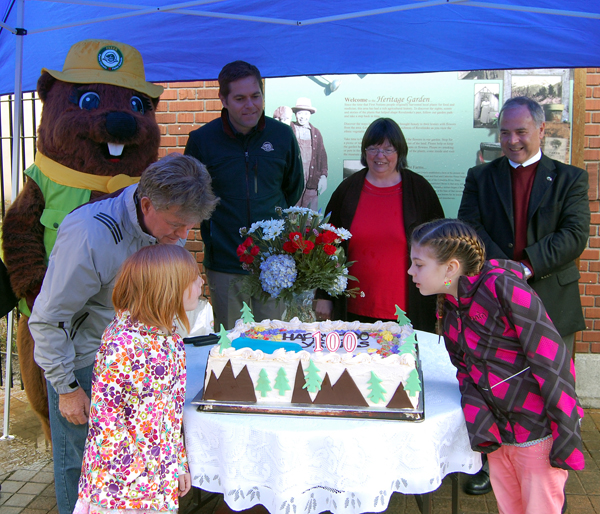 Parka the Parks Canada mascot, new Parks Superintendent Nicholas irving, Museum Curator Cathy English and Mayor David Raven as Fred Olsson encourages his granddaughters Tori and Miya Voykin to blow out the candles on the Mount Revelstoke National Park birthday cake. Fred and his granddaughters are descendants of the park's first superintendent, Frederick Edgar Maunder. David F. Rooney photo