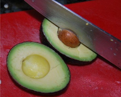 Slice the avocado in half lengthwise.     The stone will remain in one half when you cut it apart. Whang a large knife into the centre of the stone—the knife will embed in the stone, and you can easily remove it. Be careful taking the stone out of the knife. Then cut each half into three, and peel away the skin. Leslie Savage photo