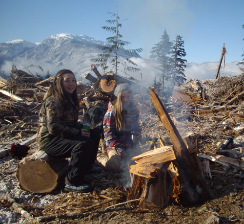 Two of the young lichen pickers warm up at a fire. The project held a number of lichen-picking expeditions and will held more this year. Although the nine cows currently in the pen will be released into the wild with their calves in mid-July, the project will continue next year. Photo courtesy of the Caribou Maternity Penning Project