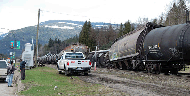 Review reporter Alex Cooper (far left) talks with retired CPR employee George Hopkins who witnessed this derailment in downtown Revelstoke on Thursday, April 2, at about 2:45 pm. "My son and I... saw this car start to go over and heard the crashing and banging as it did that," he said. "We called CP and reported it." George said the train "wasn't moving very fast and all of a sudden that car just flopped right over." The car immediately behind it also jumped the track. David F. Rooney photo