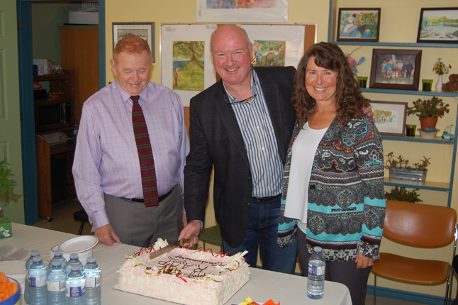 Mayor Mark McKee, flanked by Peter Waters and Laurie Rogers, slices the birthday cake created by the Modern Bakery to mark the 10th anniversary of the Revelstoke Awareness and Outreach Program on Wednesday, September 30. The program's true birthday is in November but the early fall weather put everybody in a celebratory frame of mind. David F. Rooney photo